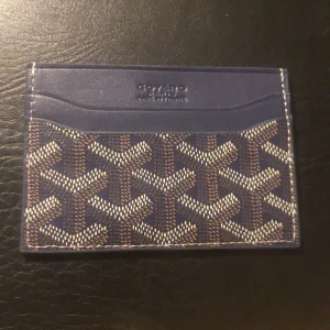 Blå korthållare - Säljer en snygg blå korthållare med ikoniska mönster i vitt och beige. Tillverkad i skinn och har flera kortfack. Kommer med original gul fodral. Perfekt för dig som vill ha något stilrent och exklusivt i fickan.