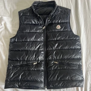 Mörkblå Moncler Gui Väst - Hej! Säljer nu min mörkblå moncler gui väst i size 4. Riktigt fint skick, bortsett från att ena ledaren till dragkedjan är borta. Den går fortfarande att zippa, men det kan vara lite svårare att få på dragkedjan, därav priset. 100% äkta, legitcheckad privat. Ni kan skicka in den på äkthetskontroll vid tveksamheter! Tveka inte med att skriva vid frågor eller funderingar. // Oskar