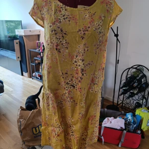 Gul blommig linneklänning - Superfin gul kortklänning i linne med blommigt mönster. Avslappnad passform med korta ärmar och rund halsringning. Perfekt för varma dagar när du vill känna dig både bekväm och snygg.