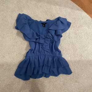 Blå volangblus från H&M - Supersöt blå blus från H&M med volanger längs halsringningen och nertill. Offshoulder-modell med elastisk midja som ger en snygg siluett. Perfekt för dig som gillar romantiska detaljer och flowy vibes. Passar mig med XS/S!💕