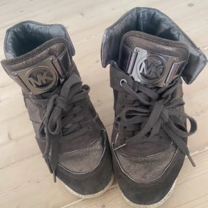 kilklack sneakers från MK - snygga bruna kilklack sneakers från Michael Kors med metallic-detaljer och stort MK-logo på plösen. skorna har snörning, rund tå och är gjorda i en mix av skinn och mocka. köpte dem för 350 och knappt använt dem, pris kan definitivt diskuteras!