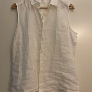Vit ärmlös linneskjorta från Uniqlo - Säljer en stilren vit skjorta från Uniqlo i luftig linne. Skjortan är ärmlös med klassisk krage och knäppning framtill. Perfekt för varma dagar när du vill ha en clean och avslappnad look.