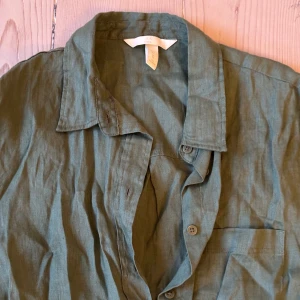 Grön linneskjorta från H&M, XS - Snygg grön skjorta i 100% linne från H&M. Skjortan har klassisk krage, lång ärm och knäppning framtill. Perfekt oversized känsla och en bröstficka för extra stilpoäng. Passar dig som gillar en avslappnad och trendig look.