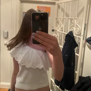 Vit oneshoulder topp från Zara - Superfin vit oneshoulder topp från Zara med volang och broderade blommor längs kanten. Toppen är ribbad. Storlek 164 men passar även om du har XSS-S!