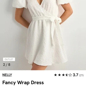Vit omlottklänning från Nelly - Superfin vit kort omlottklänning från Nelly med puffiga korta ärmar och knytband i midjan. Klänningen har en strukturerad yta och v-ringning. Nypris 499kr