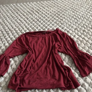 Vinröd topp med trumpetärm b.young - Vinröd topp från b.young i mjuk bomull med snygga trumpetärmar och lätt rynkade detaljer vid ärmslut. Rund halsringning och relaxed fit gör den både chill och trendig. Perfekt för dig som gillar en enkel men ändå cool stil.