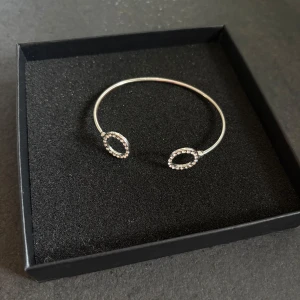 Silverfärgat armband med glittriga detaljer - Stilrent armband i silverfärg med två öppna ovala former dekorerade med små glittrande stenar. Perfekt accessoar för att lyfta din outfit med lite extra bling. Enkel och modern design som passar till många stilar.💖💖💖💖