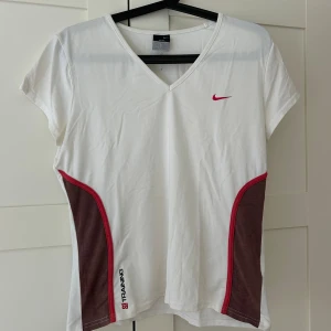 Nike Dri-Fit vit träningst-shirt  - Nike Dri-Fit t-shirt i vitt med röda detaljer och bruna paneler på sidorna. Kortärmad modell med v-ringning och sportig passform. Perfekt för träning, med ventilerande material och snyggt broderad Nike-logga på bröstet. Passar S-L beror på hur man vill att den ska sitta