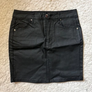 Svart kortkjol i jeans från FB Sister - Svart kortkjol från FB Sister i jeansmaterial med klassisk femficksdesign, bälteshällor och knapp framtill. Snygg och enkel modell som är lätt att matcha med allt. Perfekt för dig som gillar en stilren look.