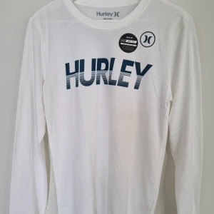 Vit långärmad t-shirt från Hurley - Oanvänd vit, tunn långärmad t-shirt från Hurley med logga framtill. Tillverkad i en mix av bomull och polyester med Nike Dri-Fit-teknologi. 