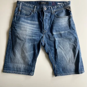 Blå jeansshorts från Replay - Snygga blå jeansshorts från Replay med klassisk femficksdesign och slitna detaljer. Shortsen har normal passform, bälteshällor och dragkedja. Perfekta för sommardagar och ger en avslappnad vibe till din outfit. Storlek w30, säljer för 300kr