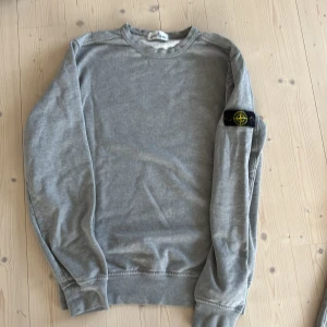 Grå Stone Island Junior sweatshirt, strl 170 (xs) - Grå sweatshirt från Stone Island Junior med klassisk rund hals och ikonisk logga på vänster ärm. I mycket fint skick. 