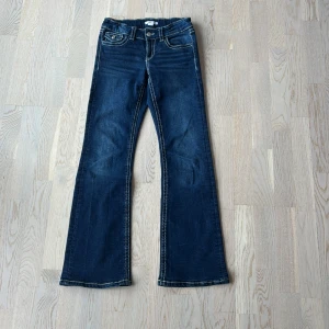 Bootcut jeans - Snygga mörkblå jeans från Ginatricot med bootcut-modell och markerade kontrastsömmar i vitt. Jeansen har en cool fickdetalj med lock och knapp framtill. Perfekta för en trendig vardagslook. Jeansen är mycket använda men fortfarande i fint skick!