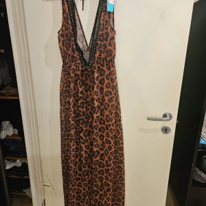 Leopardmönstrad badklänng H&M - Snygg badklänning från H&M med leopardmönster i bruna och svarta toner. Djup v-ringning med dekorativa svarta band längs urringningen och knyt i nacken. Perfekt för dig som vill sticka ut med en djurisk look.