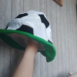Fotbollshatt med grön kant - Rolig och mjuk hatt formad som en fotboll med svartvita fält och bred grön kant. Perfekt accessoar för fotbollsfans som vill sticka ut på match eller fest. Tillverkad i syntetmaterial med plyschkänsla. One size.