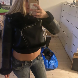 Svart pälsfodrad skinnjacka - Säljer en svart, croppad skinnjacka med pälsfoder och pälsdetaljer vid krage, ärmslut och nederkant. Jackan har sned dragkedja, två spännen vid kragen och en cool bikerstil. Perfekt för dig som vill ha en edgy look i höst och vinter. Helt oanvänd. Nypris över 800