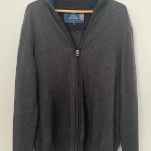 Mörkgrå kofta / Carl William  - Mörkgrå kofta från Carl William i storlek L. Klassisk modell med hel dragkedja framtill, ribbad krage och långa ärmar. Perfekt för lager-på-lager och enkel att matcha med det mesta. Mjuk och skön gjort av något slags bomull 