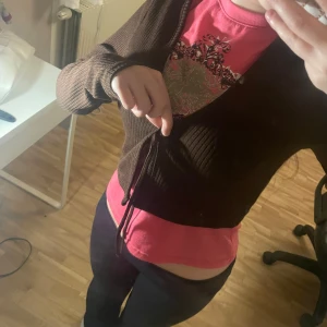 Brun ribbad omlottkofta med knyt - Säljer en brun ribbad omlottkofta med knyt i midjan. Koftan är croppad och har långa ärmar, perfekt att slänga över en topp. Materialet är mjukt och stretchigt, vilket gör den superbekväm och lätt att styla till olika outfits.