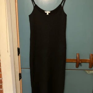 Svart långklänning från H&M - En svart långklänning från H&M med smala axelband och lätt strukturerat tyg. Klänningen har en rak passform och är ärmlös, perfekt för en stilren look. Enkel och tidlös design som funkar till många tillfällen.