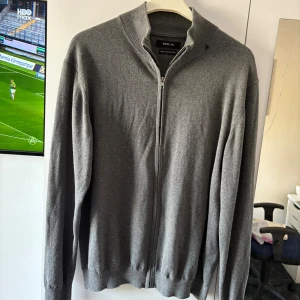 Grå kofta med dragkedja från Replay - Snygg grå kofta från Replay i återvunnen bomull. Modellen har hel dragkedja framtill, ribbad krage och muddar vid ärmslut och nederkant. Perfekt för lager-på-lager och enkel att matcha med det mesta. Klassisk och stilren design.