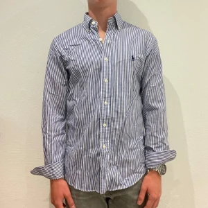 Randig Ralph Lauren Ralph Lauren skjorta - Vit/ blå randig Ralph lauren skjorta || Storlek S (Slim Fit) || Skjortan är i bra skick || Mitt pris 599kr || Modellen på bilden är 170cm och väger 62kg || Tveka inte på att höra av dig vid frågor eller funderingar 