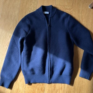 Mörkblå stickad kofta från Mango - Snygg mörkblå stickad kofta från Mango med dragkedja framtill och ribbade muddar. Perfekt för lager-på-lager och funkar lika bra till jeans som till kjol. Klassisk och enkel design med lång ärm och mjukt material.