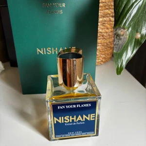 Nishane Fan Your Flames Extrait de Parfum - Exklusiv parfym från Nishane, Fan Your Flames, i en stilren fyrkantig glasflaska med guldig metallkork. Doften är exotisk med inslag av kokos, rom, tobak, tonkaböna, ekmossa och cederträ. Flaskan rymmer 100 ml och levereras i en elegant grön förpackning. Ca halva mängden kvar