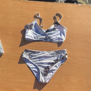 Vit och svart ljus blå, bikini från SHEIN - Snygg bikini från SHEIN i vitt med svart mönster och ribbad struktur. Överdelen har omlott-skärning och smala axelband, medan underdelen är klassisk med hög midja. Perfekt för stranden eller poolen i sommar!