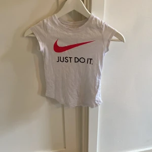 Vit Nike t-shirt med röd logga - Vit t-shirt från Nike med klassisk röd swoosh och texten 'Just Do It.' på bröstet. Kortärmad modell i mjuk bomull, perfekt för en sportig och chill stil. Enkel och clean design som funkar till det mesta. Priset diskuteras!!!