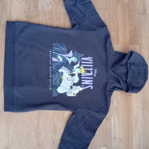 Disney Villains svart hoodie 146cm - Svart hoodie från Disney med tryck av klassiska Villains som Maleficent, Ursula och den onda drottningen. Mjuk insida, huva och lång ärm. Perfekt för dig som älskar Disney och vill ha en cool och bekväm tröja med attityd.