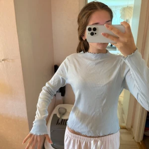 Ljusblå ribbad långärmad topp - Supersöt ljusblå/babyblå långärmad topp med ribbad struktur och vågiga kanter vid hals, ärmslut och nederkant. Perfekt för dig som gillar en enkel men ändå trendig stil. 