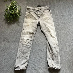 Grå jeans från Replay - Snygga grå jeans från Replay med klassisk femficksdesign och svarta detaljer på bakfickorna. Jeansen har en rak passform och är tillverkade i mjukt denimtyg. Perfekta för dig som gillar en avslappnad men stilren look.