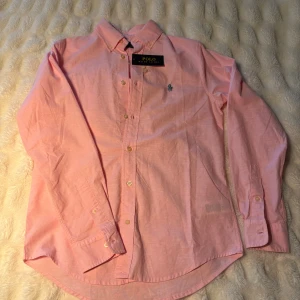 Rosa linne skjorta - Snygg rosa linne skjorta från Polo Ralph Lauren med klassisk krage och broderad logga på bröstet. Skjortan har långa ärmar, knappar framtill och är tillverkad av linne. Nypris, ca 2200kr, bara att höra av er vid funderingar!
