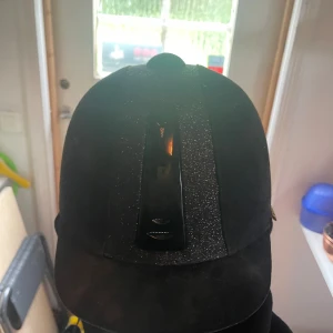 Svart ridhjälm Kylin strl 58 - Snygg svart ridhjälm från Kylin med glittrig detalj framtill och matt finish. Hjälmen har justerbart hakband. Perfekt för dig som vill ha stil på ridbanan och samtidigt känna dig säker. Säljer då jag slutat med ridning och inte använder den