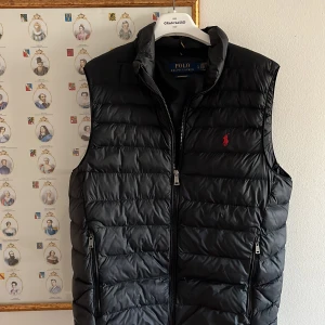 Väst | Polo Ralph Lauren - Snygg svart dunväst från Polo Ralph Lauren med dragkedja och broderad logga i rött. Perfekt för vår och höst kvällar. Västen är väldigt eftertraktad så slå till fort. Var inte rädd för att ställa fler frågor svarar snabbt. Mvh Hugo