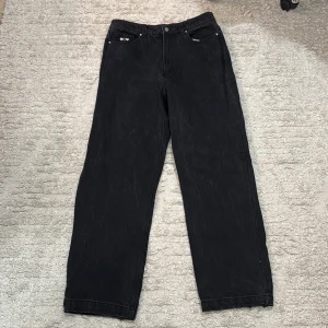 Svarta wide jeans från Nude Project - Svarta jeans från Nude Project med bred passform och coola detaljer som broderade hjärtan i guld och vitt vid fickorna. Baksidan har en rå kant med broderad Nude Project-logga. Materialet är klassisk jeans och dragkedjan har en unik Nude-etikett.