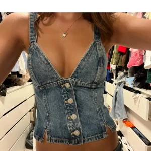 Jeans korsettopp med knappar - Snygg jeansblå korsettopp från Gina Tricot. Strl S. Toppen har knappar framtill, markerad midja och små slitsar nertill. Baksidan har smock för extra stretch 