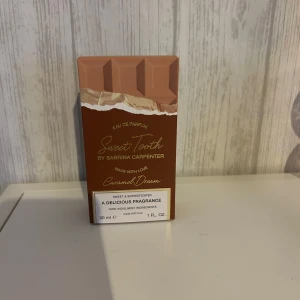 Sweet Tooth Caramel Dream parfym - Parfymen Sweet Tooth Caramel Dream från Sabrina Carpenter kommer i en unik chokladkakeformad flaska i bruna och beige toner. Doften är söt och sofistikerad, perfekt för dig som älskar gourmanddofter. Flaskan rymmer 30 ml och har en modern, lekfull design.