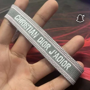 Grått armband från CD - Snyggt vävt armband vitt. Armbandet är grått med ljusa detaljer och har justerbar knytning med två tofsar. Perfekt accessoar för att lyfta din outfit med en lyxig touch.