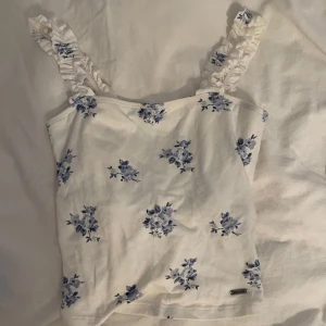 Vit blommig linnetopp med volangband - Supersöt vit linnetopp med blått blommönster och volangprydda axelband. 🐚🌊