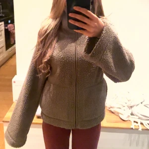 Brun teddyjacka från hm - Mysig beige teddyjacka med hög krage och dragkedja framtill. Jackan har en loose passform och långa ärmar, perfekt för kyliga dagar. Tillverkad i fluffigt fleece-material som ger en skön och avslappnad vibe.