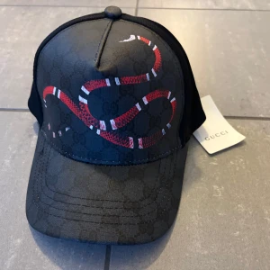 Svart keps med röd orm - Säljer en svart keps med ikoniskt GG-mönster och en fet röd och vit orm på framsidan. Kepsen har böjd skärm och mesh på baksidan för extra ventilation. Snyggt tryck på insidan och justerbar rem baktill. Också köpt av en kompis inget bevis därav pris:)
