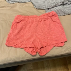 Korallrosa shorts från Lindex - Snygga korallrosa shorts från Lindex i mjuk bomull. De har elastisk midja och öppningar för snörning, vilket gör dem extra bekväma. Perfekta för varma dagar och chill häng. Färgen är riktigt fräsch och modellen är loose fit för skön känsla.