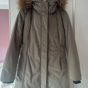 Ny. Beige parkas med äkta päls - Säljer en ny Boss Hugo  beige dunjacka med lång passform och huva med äkta päls. Jackan har långa ärmar, dold dragkedja och stilrena sömmar längs sidorna. Perfekt för kalla dagar med sin varma och skyddande design. Jacka köpt på en butik Cirkus på Väla. Kostade 6000kr. Bröst 108cm, längd 94cm, ärmar 68cm. Kommer att filma hela processen, när jag packar och skickar jacka.