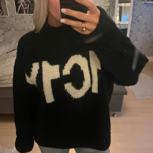 Svart stickad polotröja med text - Säljer en svart stickad polotröja med vit, stor text framtill. Tröjan är oversized med lång ärm och hög krage, perfekt för dig som gillar en chill och trendig vibe. Mjuk och mysig känsla, passar grymt till jeans eller kjol.