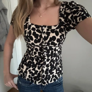 Leopardmönstrad blus med knappar - Supersnygg blus med svart leopardmönster på beige botten. Blusen har korta puffärmar, markerad midja och knappar framtill. Fyrkantig urringning ger en trendig vibe och materialet känns lätt och bekvämt.