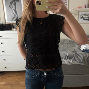 Svart blus med broderade blommor Zara - Supersöt svart blus från Zara med broderade blommor och hålmönster. Blusen har korta ärmar med volang och rund halsringning. Perfekt att styla med jeans eller kjol för en trendig look.