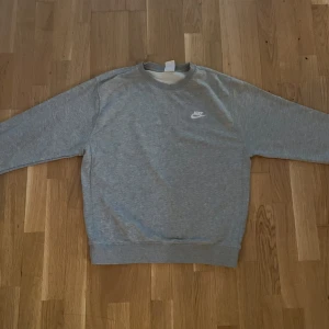 Grå Nike sweatshirt i bomull - En stilren grå sweatshirt från Nike med klassisk logga på bröstet. Tröjan har rund halsringning, långa ärmar och ribbade muddar. Perfekt basic-plagg i mjuk bomull som funkar året runt. Enkel att matcha med jeans eller joggers.