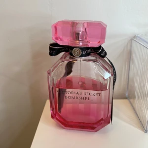 Victoria's Secret Bombshell parfym - Snygg parfymflaska från Victoria's Secret i modellen Bombshell. Flaskan är åttakantig med en rosa toning och har ett stort, rosa facettslipat lock. Dekorerad med ett svart band med VS-logga runt halsen. Perfekt för dig som gillar fräscha och feminina dofter.