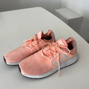Adidas rosa sneakers  - Snygga sneakers från Adidas i en ljusrosa färg med vita detaljer och klassiska ränder på sidorna. Ovandelen är i mesh för extra andningsförmåga och skon har snörning samt en vit sula med svart yttersula. Perfekta för en sportig och trendig look.